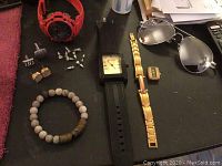Full view of all items including watches, bracelets, cufflinks, earrings, ring and sunglasses on black surface.