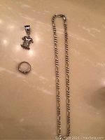 Sterling silver chain, clown charm pendant, and silver ring displayed on a beige surface.