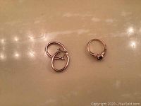 Gold-tone ring and earrings on a reflective surface, showing overall shape and details.