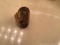 Photo showing the front face of the gold ring featuring the Buddha and red stone.
