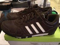 Side view of pair of brown Adidas sneakers with white stripes, atop original green Adidas box.