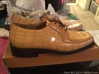 Side view of the tan crocodile patterned Florsheim men's dress shoe on box with black sole and laces.