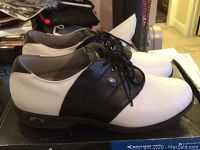 Photo of Adidas men's golf shoes from side angle showing black and white leather upper and black sole, placed on original Adidas box.