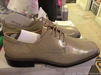 Side angle view of beige/tan Hugo Vitelli men's dress shoe, showing lace-up detail, sole design, and box underneath.
