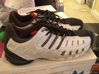 Side angled view of the Adidas sneakers showing white synthetic leather with black stripes and red detail inside heel.