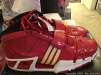 Left sneaker angled to show side stripe and sole design, red synthetic upper with strap and black interior.