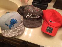 Three men's baseball hats displayed on a countertop, showing team logos and brand details.