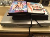 Photo showing Emerson DVD player with DVDs stacked on top, including visible titles of some movies.