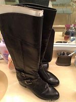 Side angle showing the full height of the black leather riding boots with buckle strap detail.