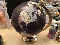 Small globe showing North America and Europe on dark blue map with beige continents, mounted on metallic base with brass-colored meridian.