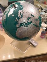 Large globe showing Europe, Africa, and part of Asia with teal oceans and silver continents, on clear acrylic stand with visible Broyhill tag.