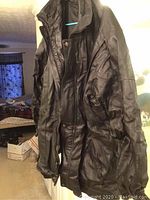 Front view of black men's leather jacket hung on a hanger showing full length and slight wear creases.