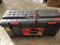 Closed black plastic toolbox with red latches and label on front.