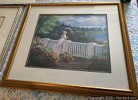 Full view of framed painting on a patterned surface showing girl in white dress on balcony with flowers and distant water scene.