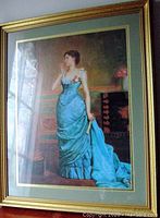 Framed print of a young woman in an aqua gown standing beside a pedestal with a cherub statue, captured in the photo showing the full frame with gold pattern and green matting.