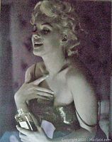 Photo showing Marilyn Monroe in glamorous attire holding a Chanel perfume bottle, looking to the side.