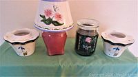 Photo showing two glass jar candles and three ceramic pieces including a ceramic top with floral painting and two matching ceramic accessories.