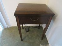 Dark wood floor stand with a front drawer, four legs, a foot pedal on the floor, and power cord.