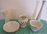 Four white vases and two white bowls arranged on a teal cloth, also includes a small glass candle holder with white candle.