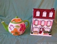 Photo showing front view of floral ceramic teapot and house-shaped cookie jar with maroon roof