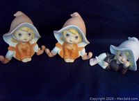 Front view of three vintage Homeco elf figurines, two with orange and white clothes and one in black and white laying down