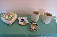 Image showing heart-shaped trinket box, small Staffordshire-style tray with blue floral decoration, McCoy white quilted sugar and creamer, and small figurine holding heart-shaped mirror on green cloth