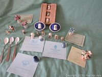 Wide view showing all thimbles, floral figurines, souvenir spoons, thimble plates, and commemorative cards laid out on a green cloth background.