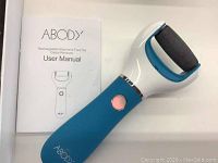Blue and white handheld electronic foot file callus remover with user manual on white surface.
