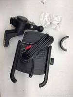Black motorcycle phone holder with attached wiring and mounting bracket, with small plastic bag containing screws and extra mounting piece.
