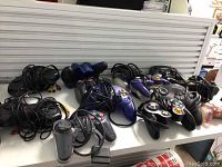 Photo showing a variety of wired and wireless game controllers in black, purple, and other colors.