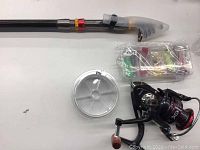 Fishing rod set components laid out showing rod, reel, bait in box, spool of line, and protector on hook keeper.
