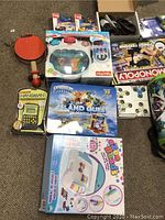 Various packaged toys laid out on floor showing electronic games, craft kits, fidget spinners, and musical toy.