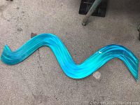Turquoise wavy abstract metal wall hanging on carpeted floor.