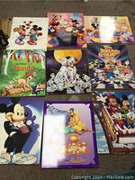 Top-down view of nine Disney wood wall art pieces laid out on a carpeted floor showing various classic Disney characters and scenes.