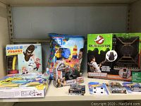Shelf with multiple packaged toys including Plush It Frenzy, LEGO Blocks, Jurassic Park, Ghostbusters, Hot Wheels, and Halo toys
