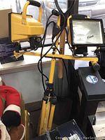 Yellow and black dual light projector mounted on tripod, with visible wiring and power cords.