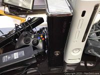 Photo showing black and white Xbox 360 consoles vertically positioned with black controller and AC adapter visible.
