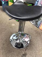 Close-up of black leather contoured seat on silver metal column and base showing height adjustment lever.
