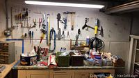 Overall view of pegboard with hand tools hanging including screwdrivers, pliers, hammers, and shears, above the workbench with plastic bins and hardware boxes on top.