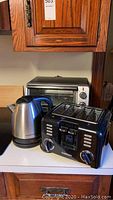 View of the toaster oven in the background, the electric kettle, and the Cuisinart toaster on a kitchen counter.