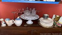 Full view of all items arranged on red shelf: milk glass cake stand, crystal sugar bowl and creamer on tray, Wedgwood plates stacked, shell motif ceramic sugar bowl and creamer, red glasses, pewter items, small figurine, and wooden serving utensils.