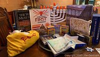 Group photo of Judaica items including matzah cover, electric menorah, Chanukah candles, and assorted books and utensils on a wooden table.
