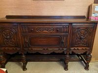 Front view of vintage buffets with carved wood doors, drawer, knobs, and turned legs.