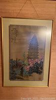 Full view of framed Asian landscape silk wall art featuring a pagoda and trees with calligraphy in the upper left corner.
