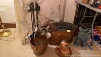 Fireplace tools stand with four tools, copper ash bucket with ceramic handle, large copper wood bucket with firewood, and vintage copper diving bell helmet on the floor.