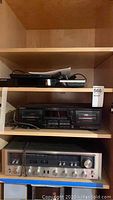 Three electronic components on wooden shelves: top a black Samsung unit, middle a Sony dual cassette deck, bottom a silver Kenwood receiver