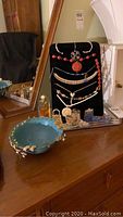 Photo showing black velvet necklace display stand with several necklaces including cinnabar pendant, beaded necklaces, and gold-tone necklace. Blue ceramic bowl and small decorative shoes and purses visible.