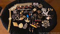 Top view of assorted costume jewelry and watches spread out on black cloth showing pins, earrings, bracelets, and wristwatches
