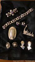 Full view of jewelry collection laid on black cloth including bracelet, pins, and earrings with purple stones and silver and gold-tone pieces.