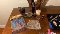Overview of lot on wooden table showing two purses, glass dish, perfume bottles, candles, lipstick, jar and jewelry